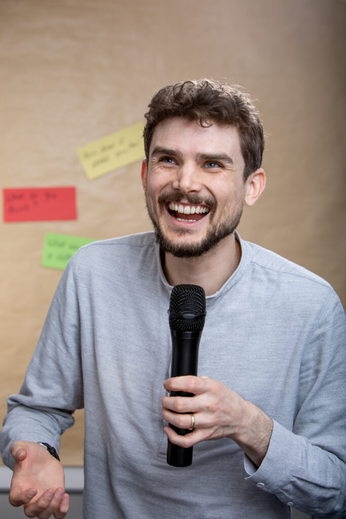 A photo of Jamie. He is holding a microphone and laughing.